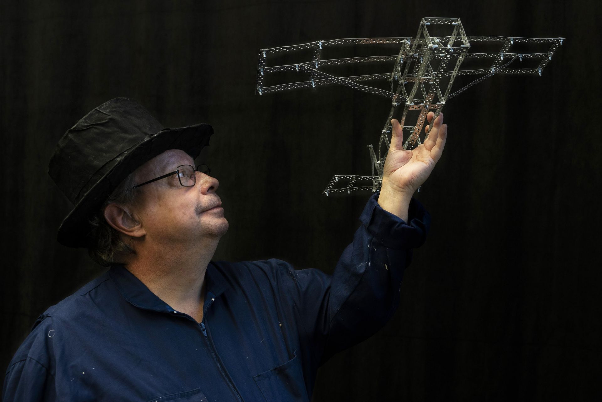 DuvTeatern actor Krister Ekebom wears a top hat, gazing towards his miniature airplane crafted from perforated steel banding.