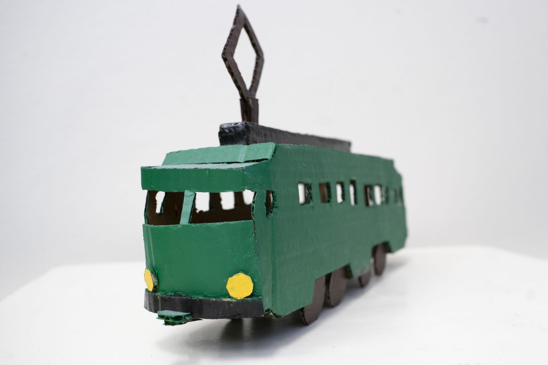 Cardboard miniature of an old Helsinki tram. The tram is painted in dark green with black and yellow detailing.